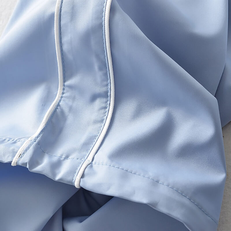 Close-up of light blue woven polyester fabric of oversized baggy high-waisted sweatpants with white trim, highlighting texture and design.